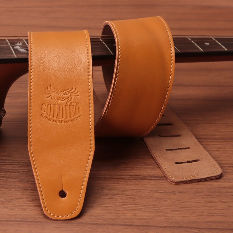 Tan Soldier double-layer cowhide guitar strap across a guitar neck, with the maker logo embossed on the end